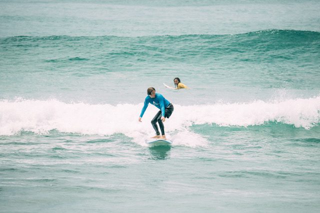 A beginner surfer catching a wave with the help of his surf instructor.