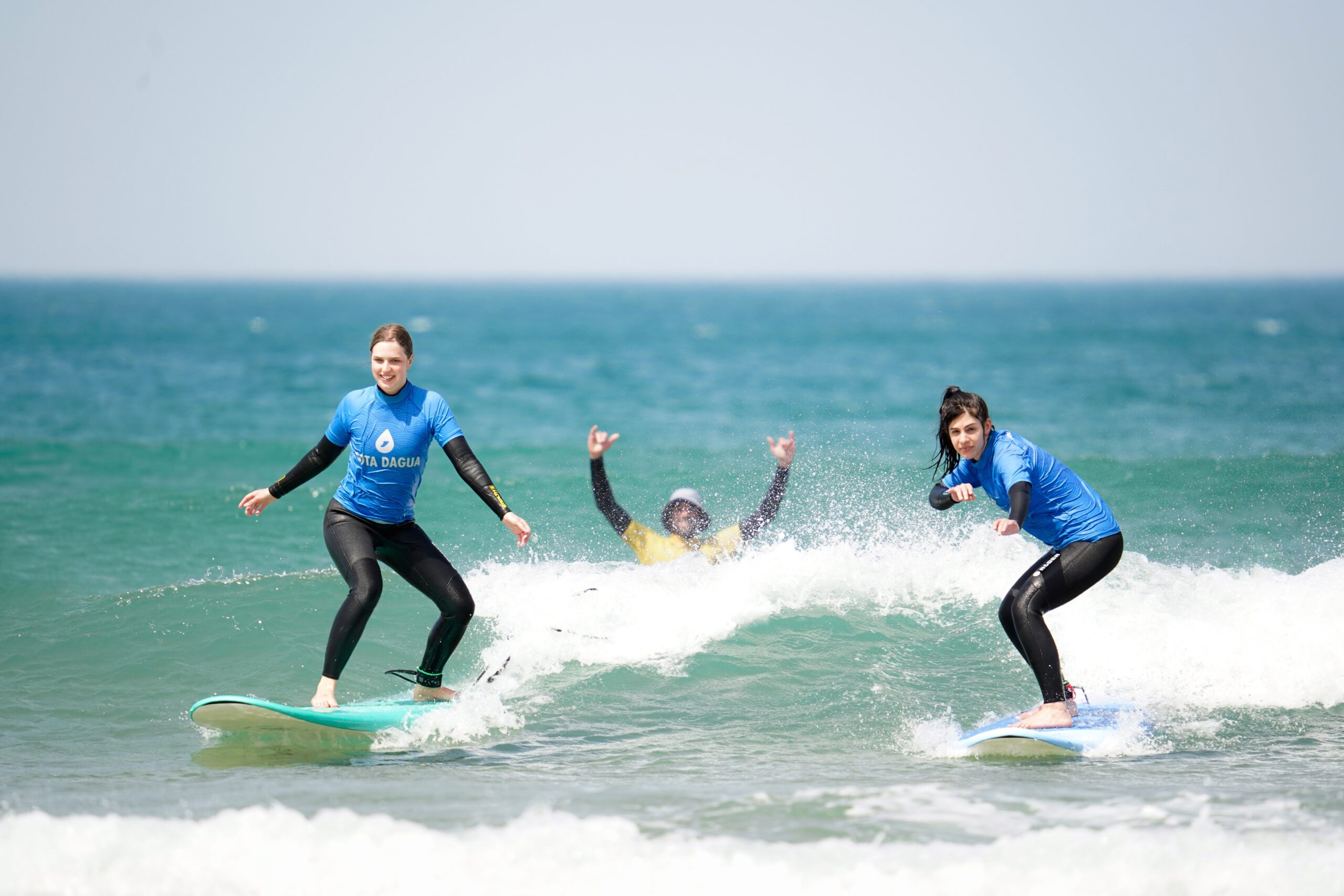two girls in surf lesson catching a wave with the help of their instructor