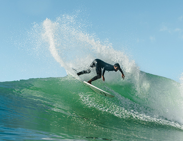 Surfer in a wetsuit making a sharp turn amid ocean spray on a green wave