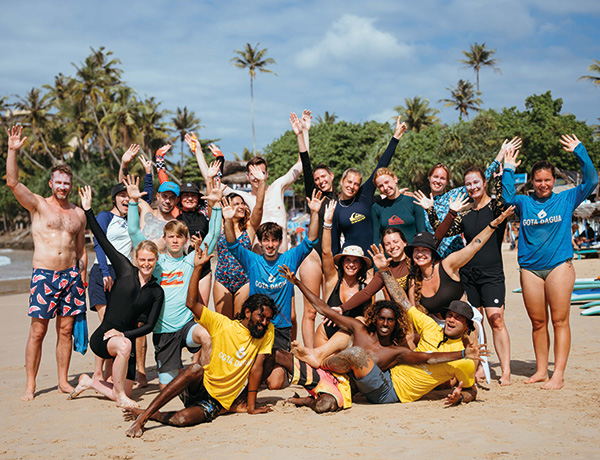 Large group of surf campers posing and cheering together on a Sri Lanka beach