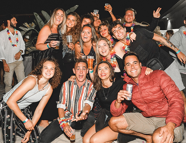 Group of smiling guests posing together with drinks at a nighttime beach party