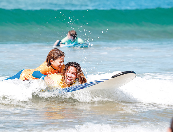 Instructor and child laughing while riding a wave together on a surfboard