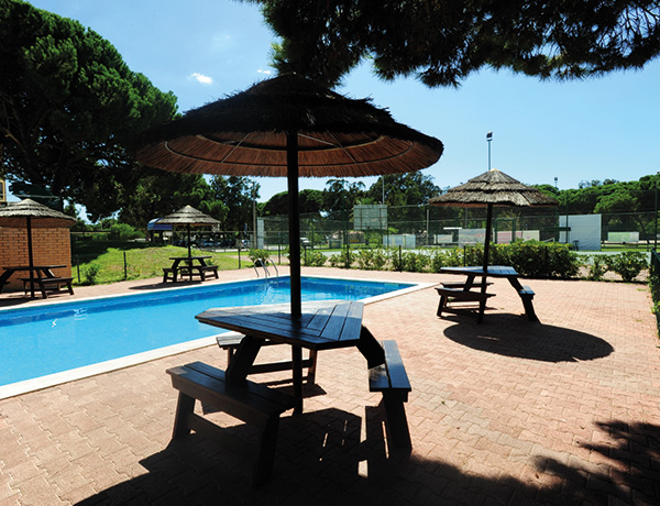 Poolside picnic tables under thatched umbrellas at our junior surf camp in Portugal