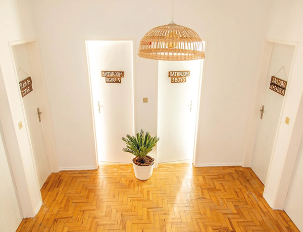 Hallway with a rattan pendant lamp and marked shower rooms in our surf camp Portugal house