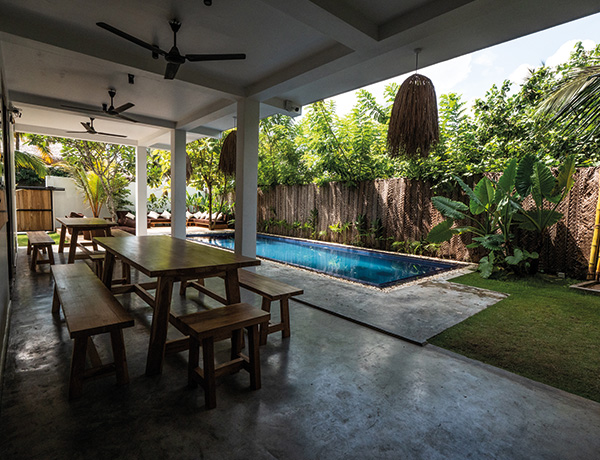 Shaded patio with wooden tables overlooking the pool and garden at our surf camp Sri Lanka