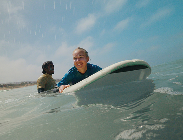 Surf instructor and smiling student holding a surfboard together in the water
