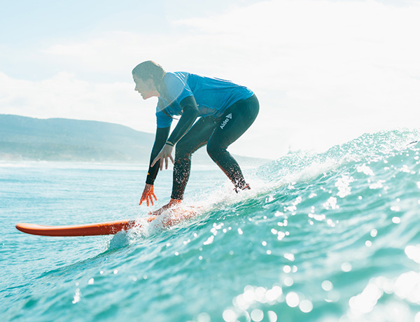 Surfer riding an orange surfboard down a wave with hills in the background