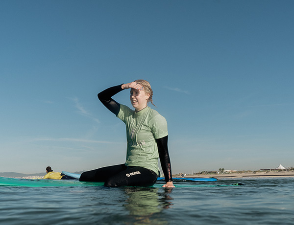 Surfer sitting on a board shielding her eyes while looking toward the shore