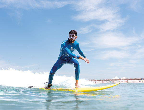 Surfer riding a small wave standing on a yellow board near a Portuguese beach