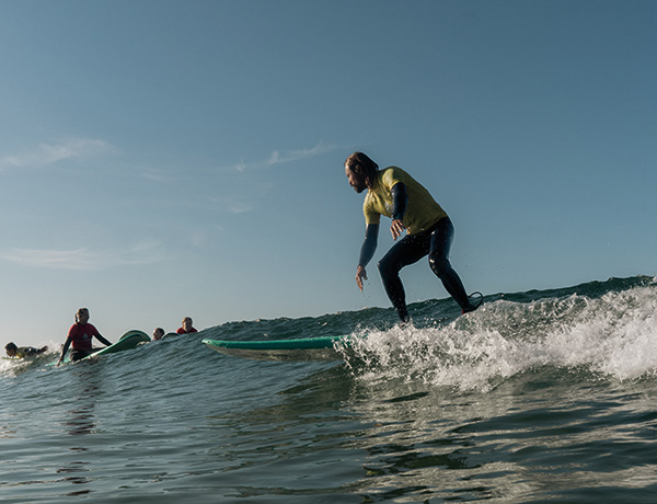 Surfer in yellow rash guard riding a wave on a green surfboard, others waiting nearby