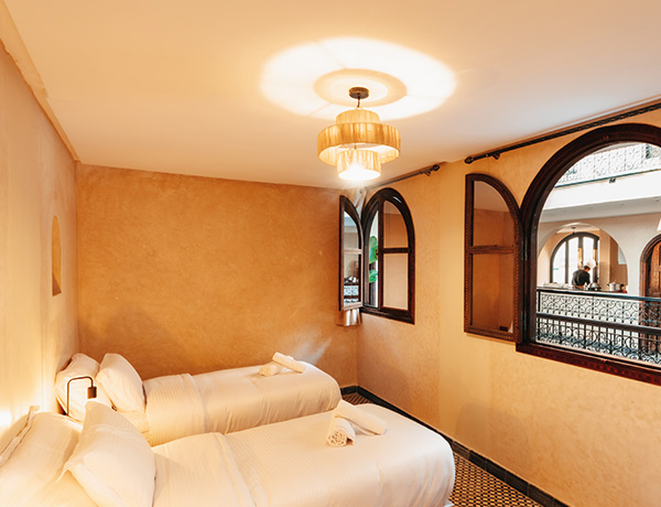 Twin bedroom with ochre walls and arched windows in our Tamraght surf camp house
