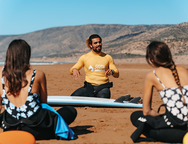 Gota Dagua instructor in a yellow rashguard briefing two seated surf students on the beach