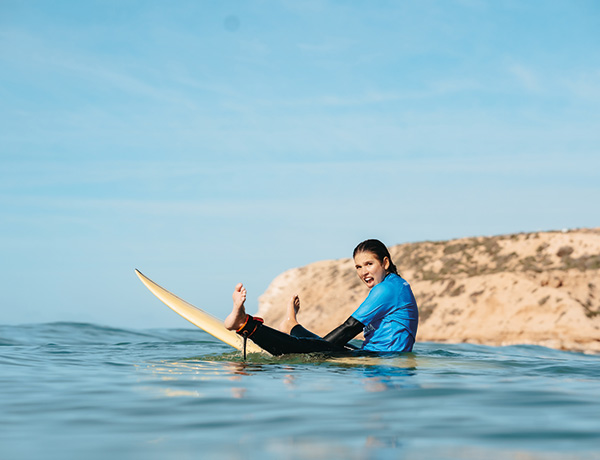 Woman laughing while sitting on a surfboard in the ocean near a coastal cliff