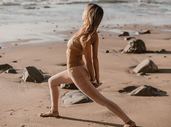 Woman stretching in a lunge pose on a sandy beach scattered with rocks