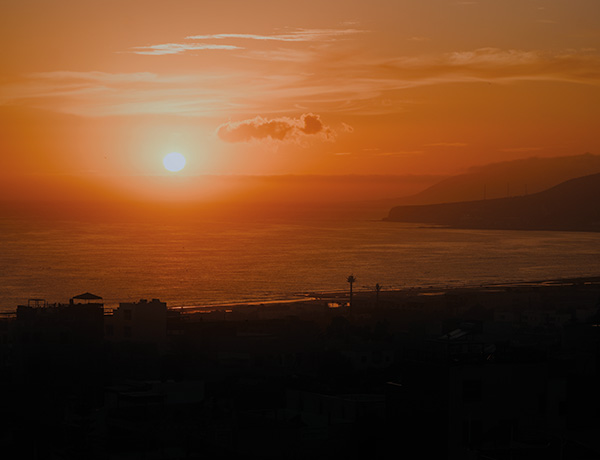 Orange sunset over the ocean with a silhouetted coastal town and hills