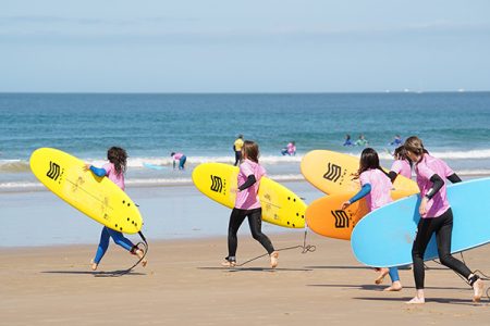 Children running along the beach with surfboards at our junior surf camp