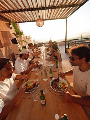Group sharing a rooftop dinner at sunset under a wooden pergola in Morocco