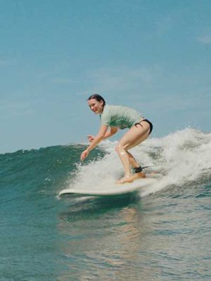 Woman in a green rash guard surfing down the face of a breaking wave
