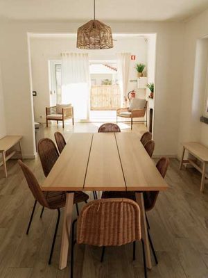 Wooden dining table with woven rattan chairs in a bright, open-plan dining room