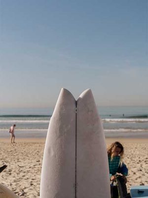 Close-up of a surfboard nose standing upright on the beach with the ocean behind