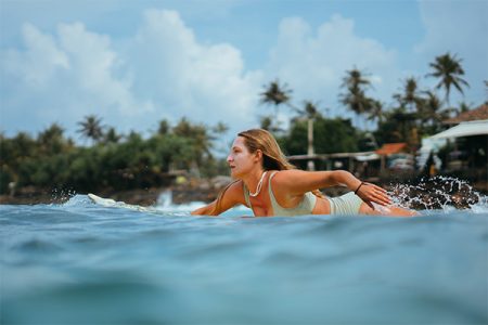 Woman paddling past a palm-lined coast at our surf camp Sri Lanka in Ahangama