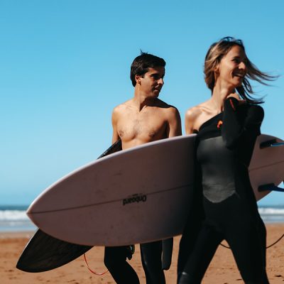 Man and woman carrying white surfboards while walking along a sunny beach