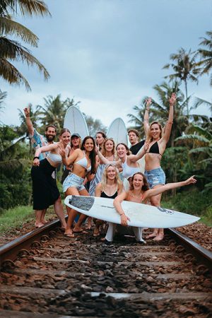 Group of surfers posing with surfboards on railway tracks lined with palm trees