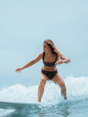 Woman in a bikini riding a wave, crouched low on a surfboard