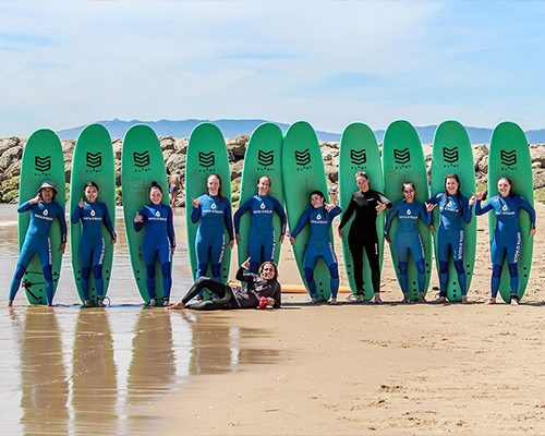 Group of surfers holding green surfboards on a beach near a rocky breakwater
